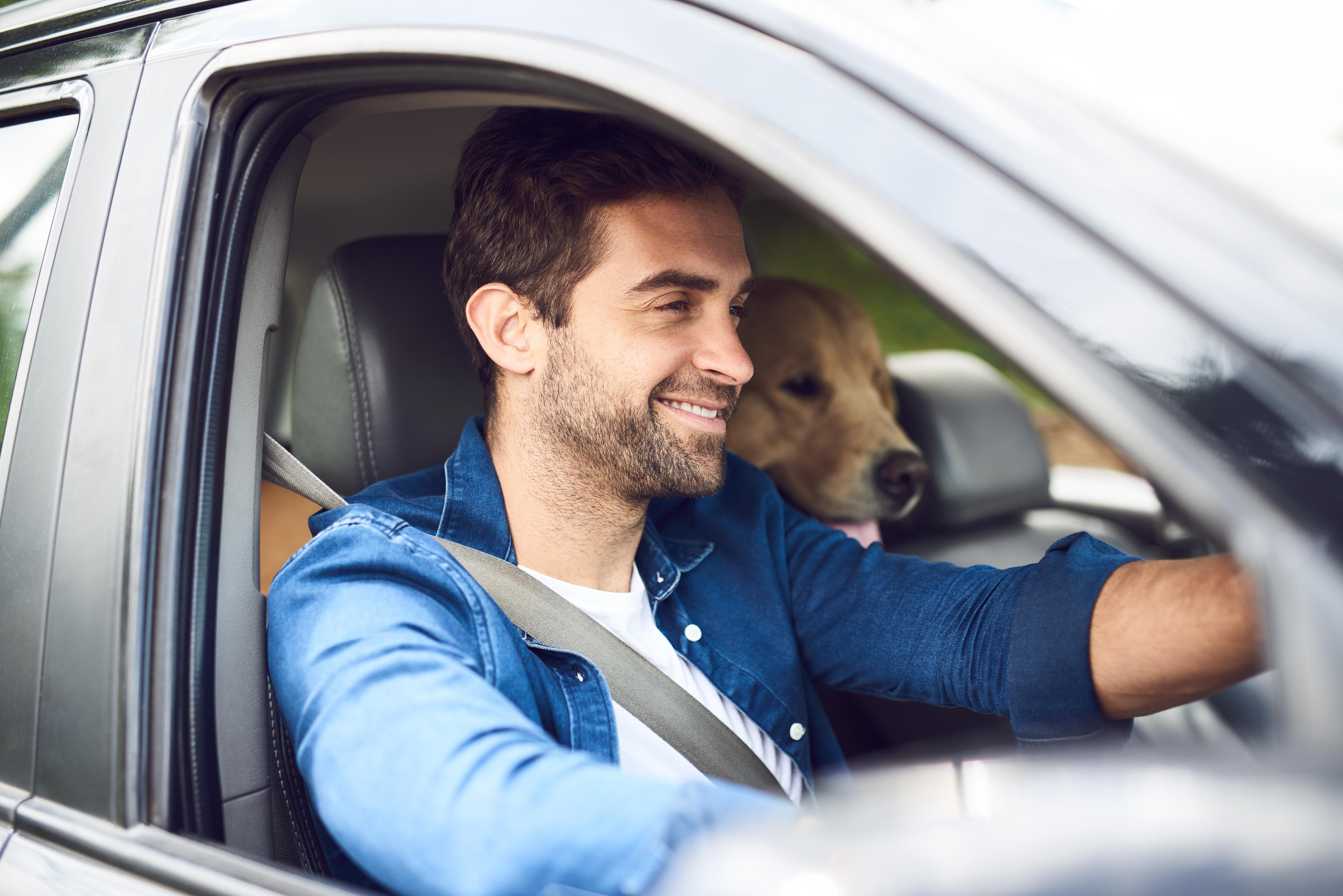 A close up of a man and a dog through the window of a car