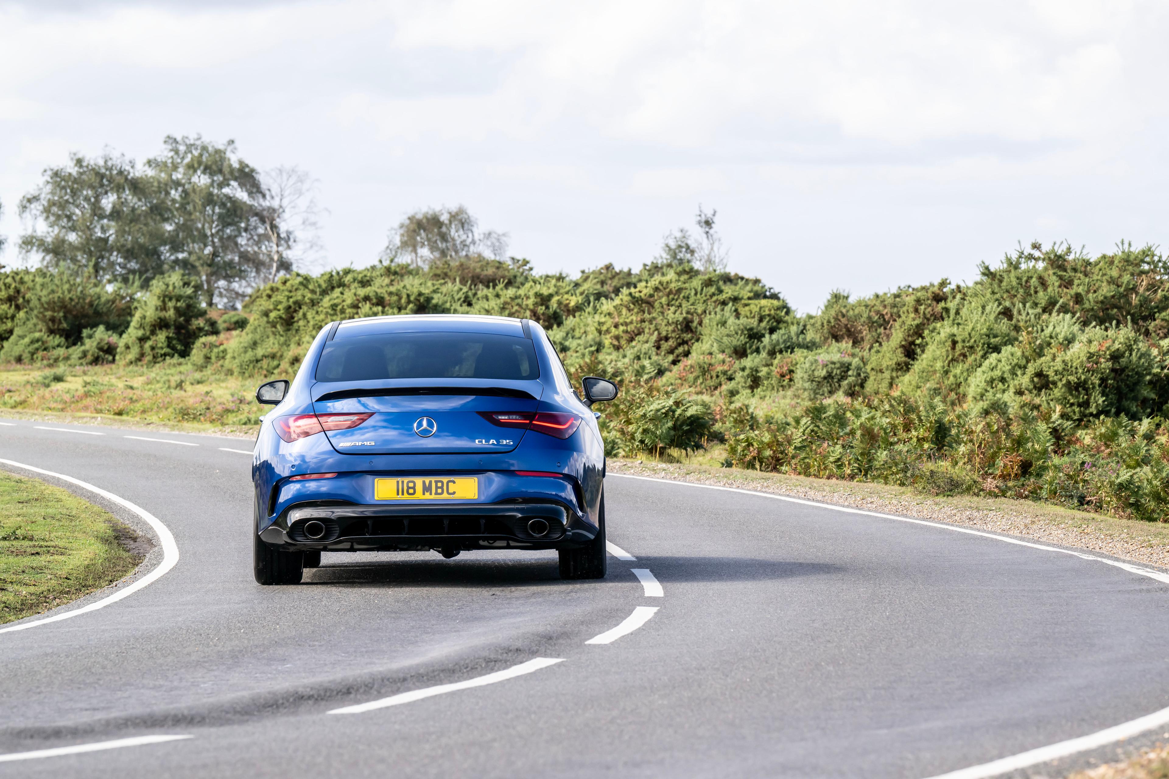 a blue mercedes-amg cla 35 driving away from the camera on a windy country road in the UK