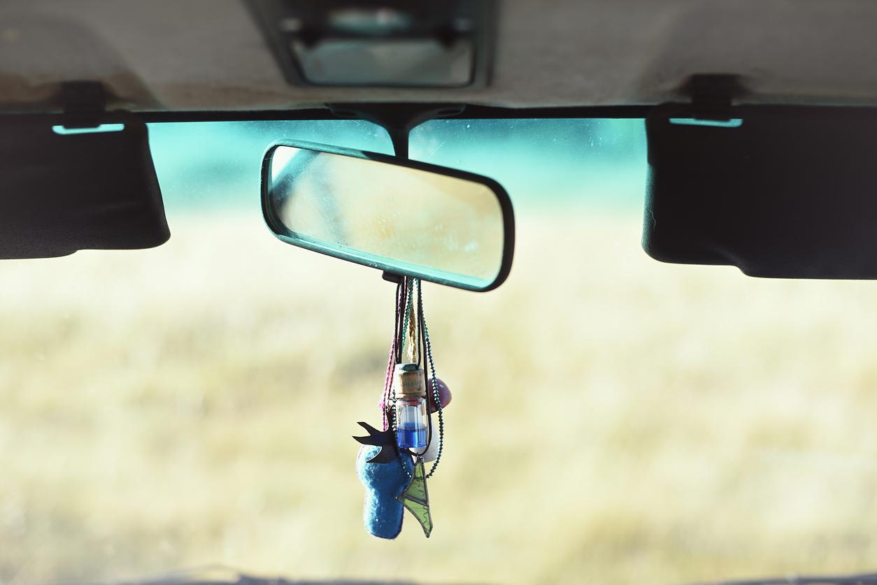 A car rearview mirror with lots of accessories and air fresheners dangling