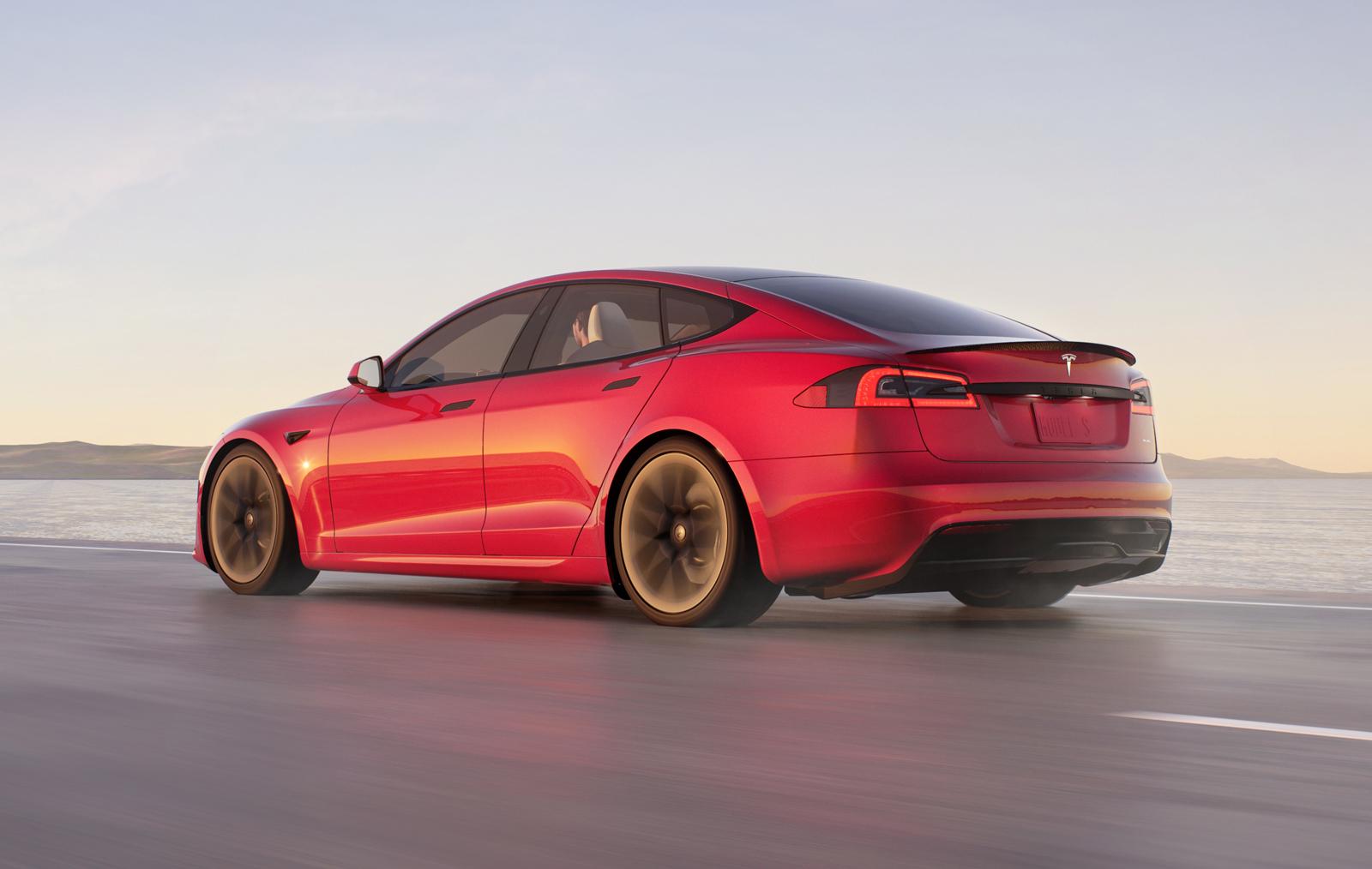 a red tesla model s plaid driving on an empty road away from the camera