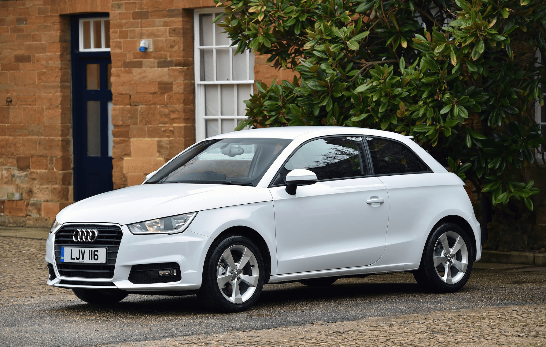 A white Audi A1 parked outside a house with bushes