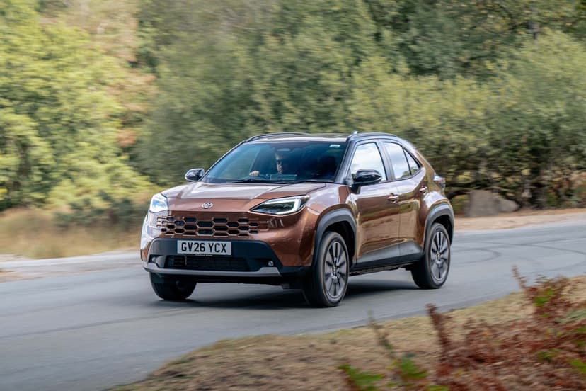 A bronze Toyota Yaris Cross driving on a rural road with blurred greenery in the background.