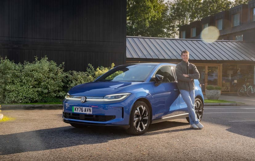 Craig Hale leans against a blue VW ID. Polo parked in front of a building, with greenery and a bicycle visible in the background.