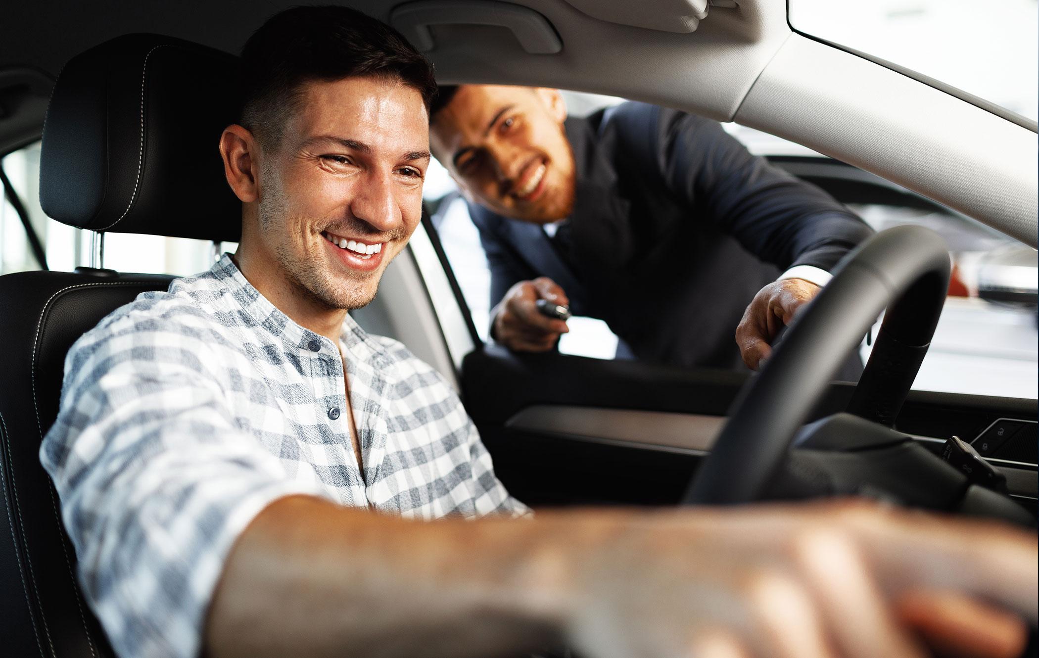 A car salesman showing a young buyer his new car