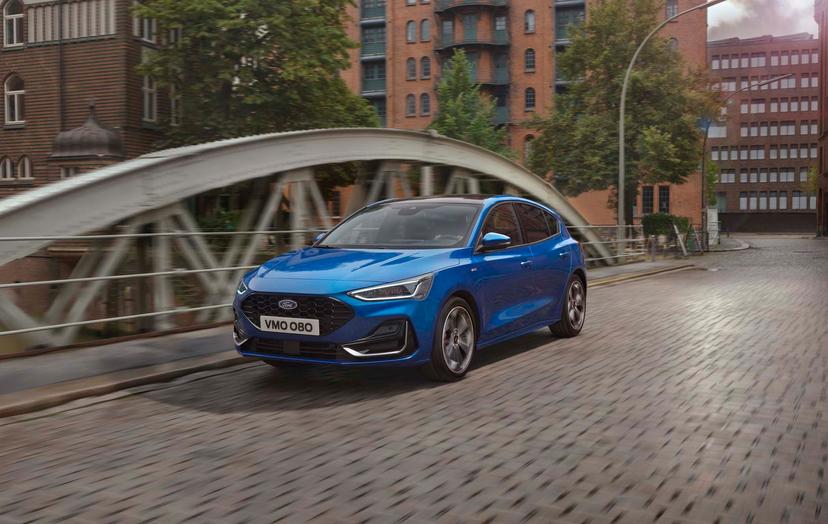 Blue Ford Focus driving on a cobblestone street with a bridge and brick buildings in the background.