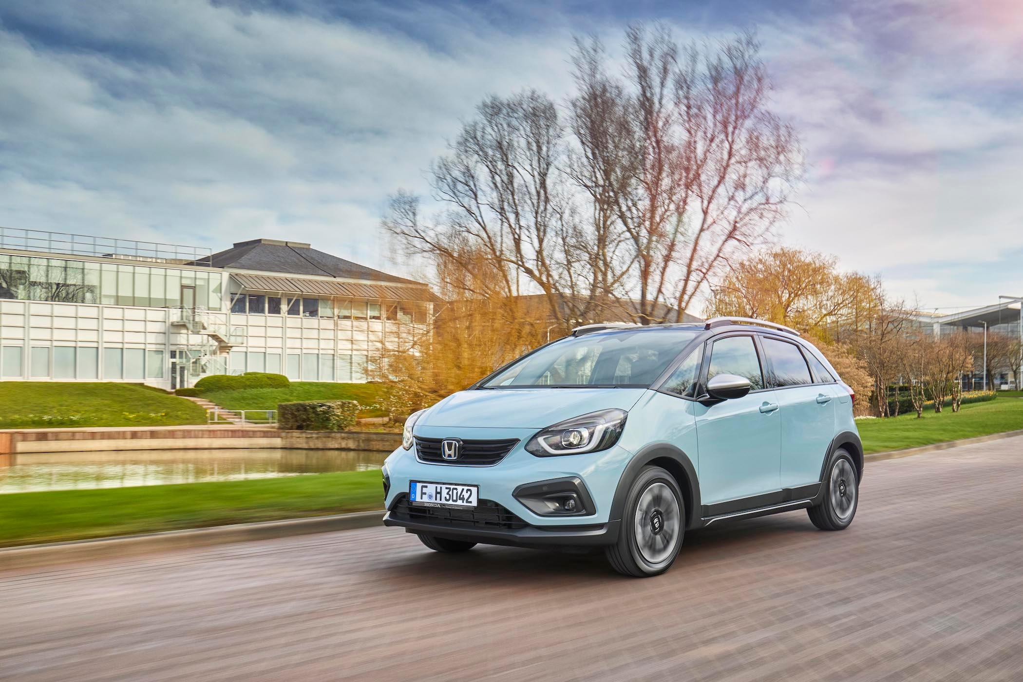 light blue honda jazz driving on a road next to a big building