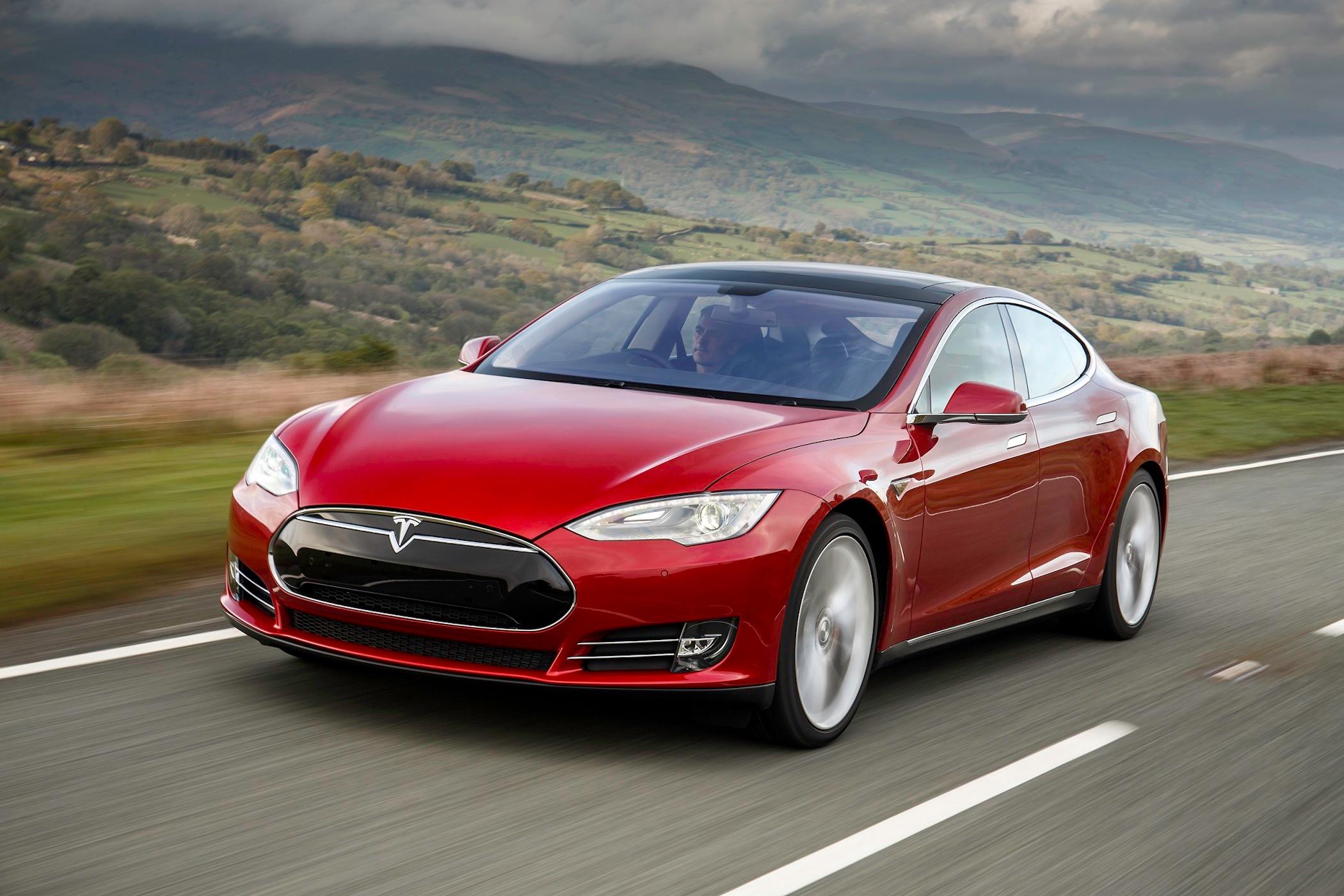 a red tesla model s driving on a road