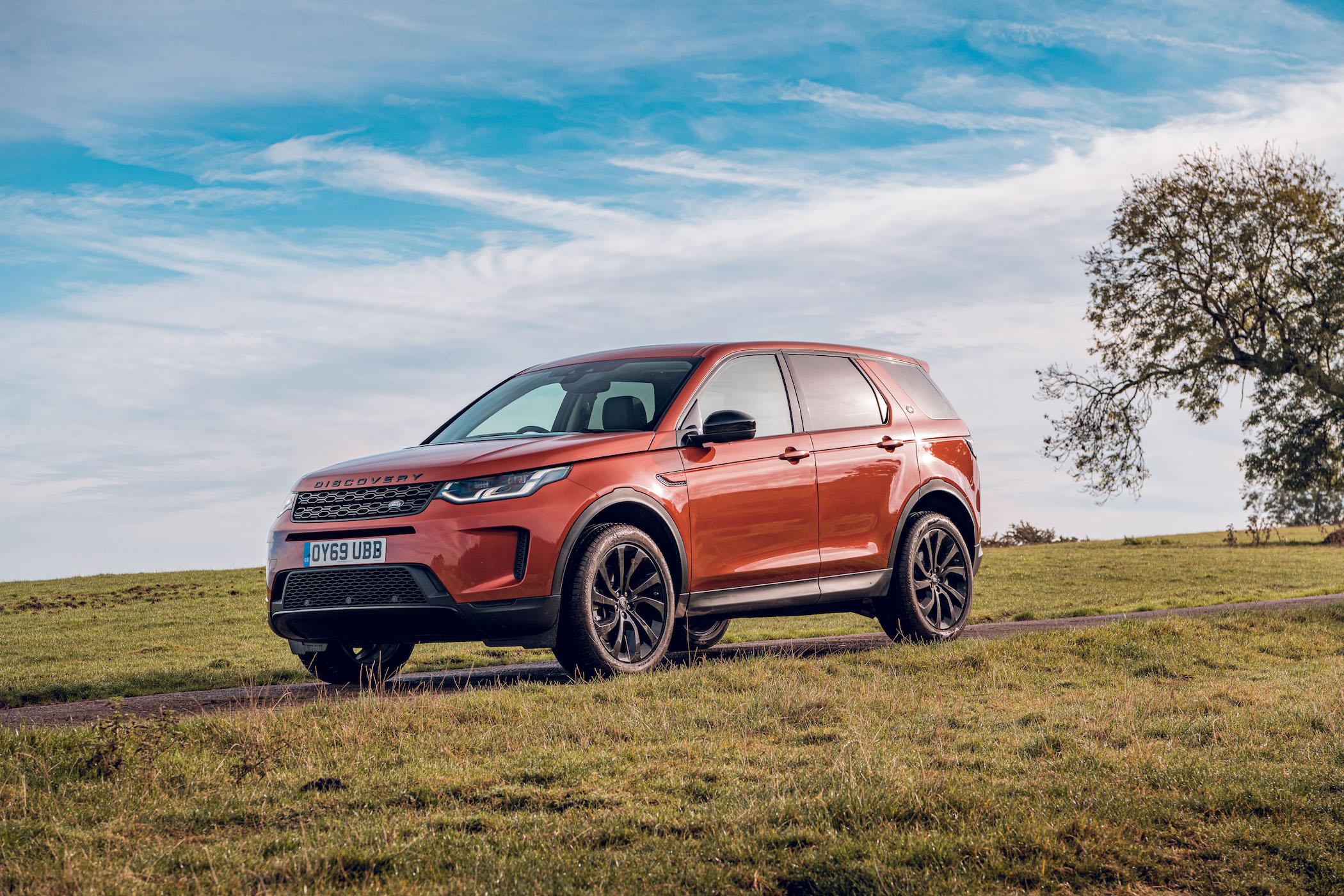 an orange land rover discovery sport parked in a field