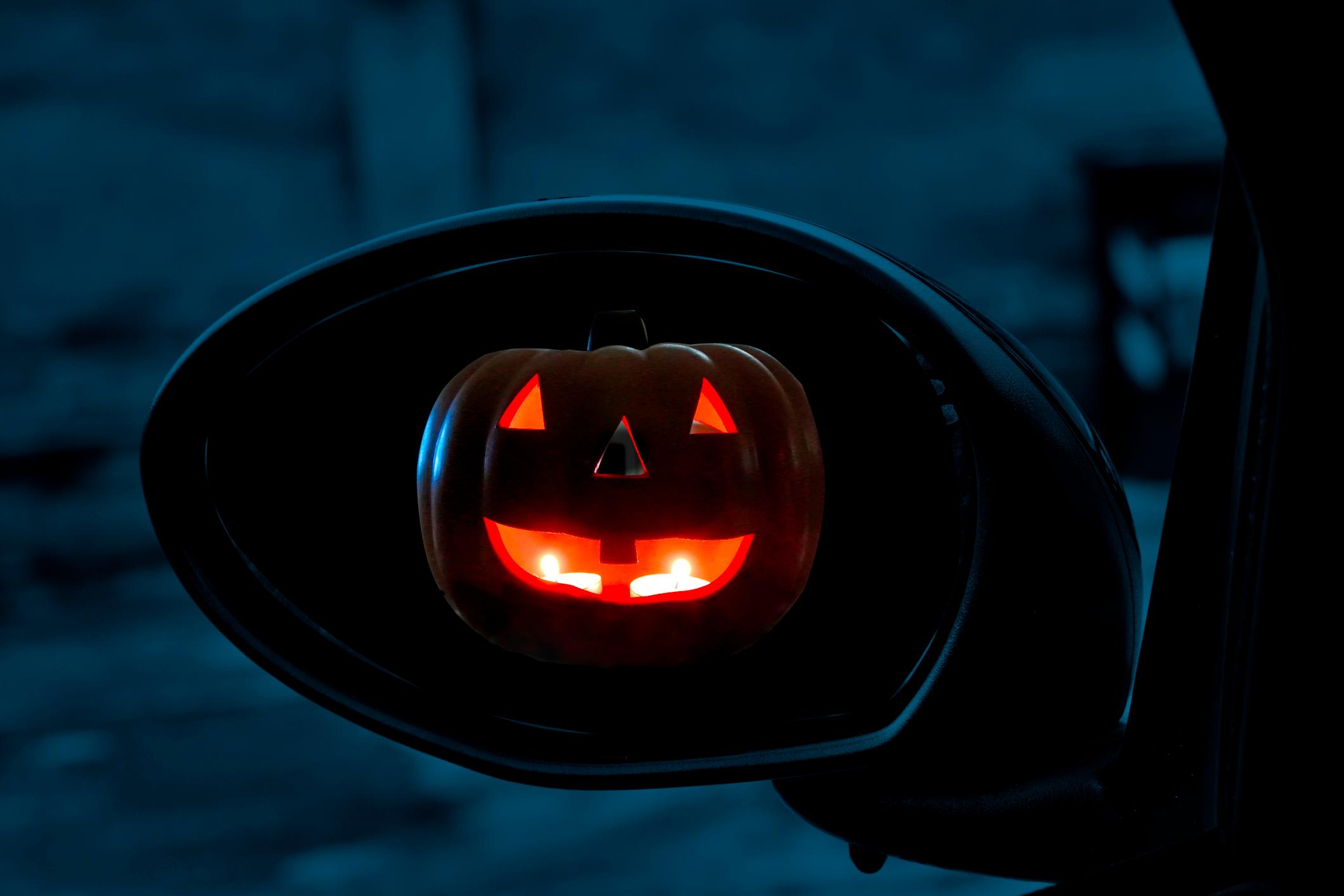 A carved pumpkin in the side wing mirrors of a car