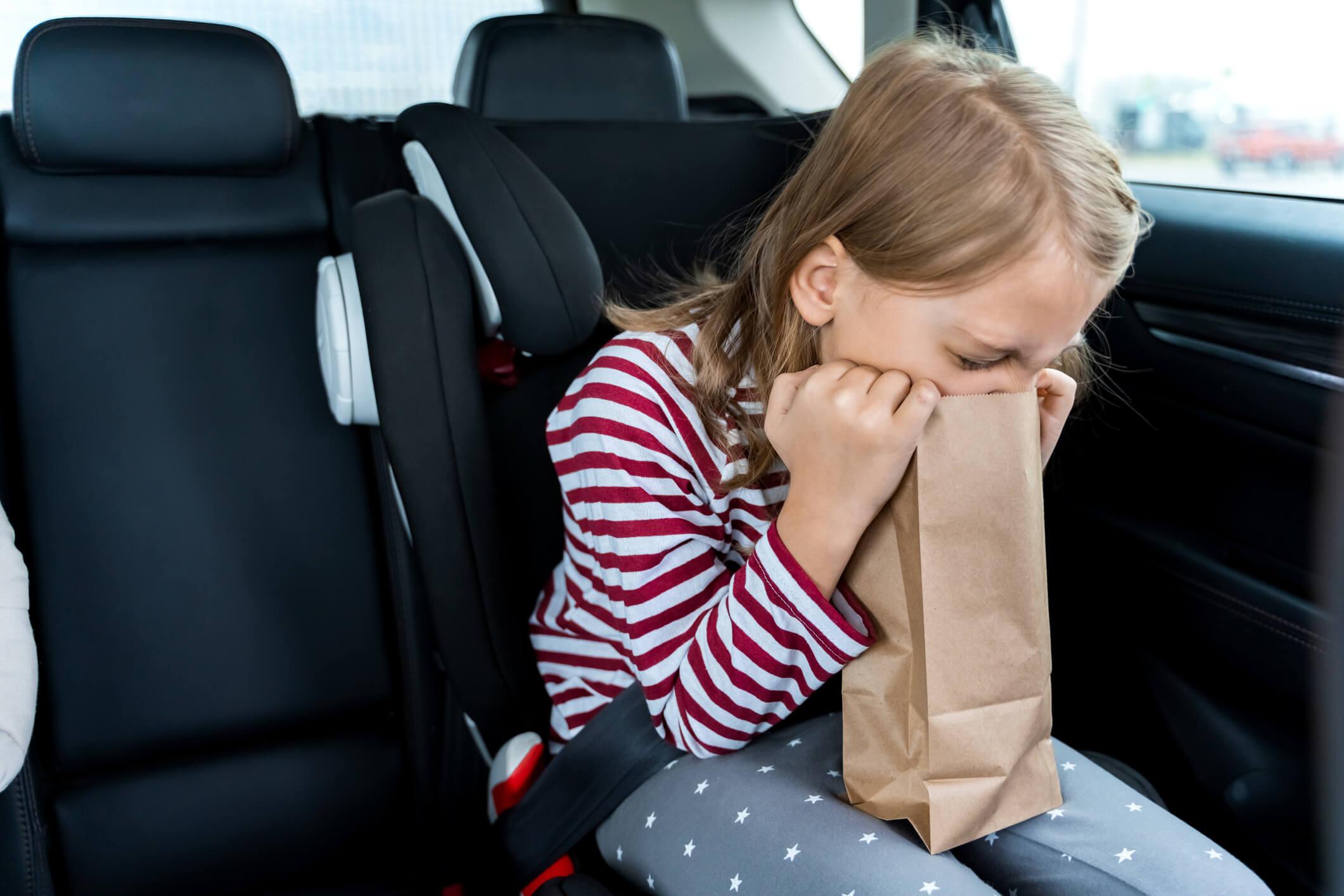 A child in a car seat holding a brown paper bag and looking unwell