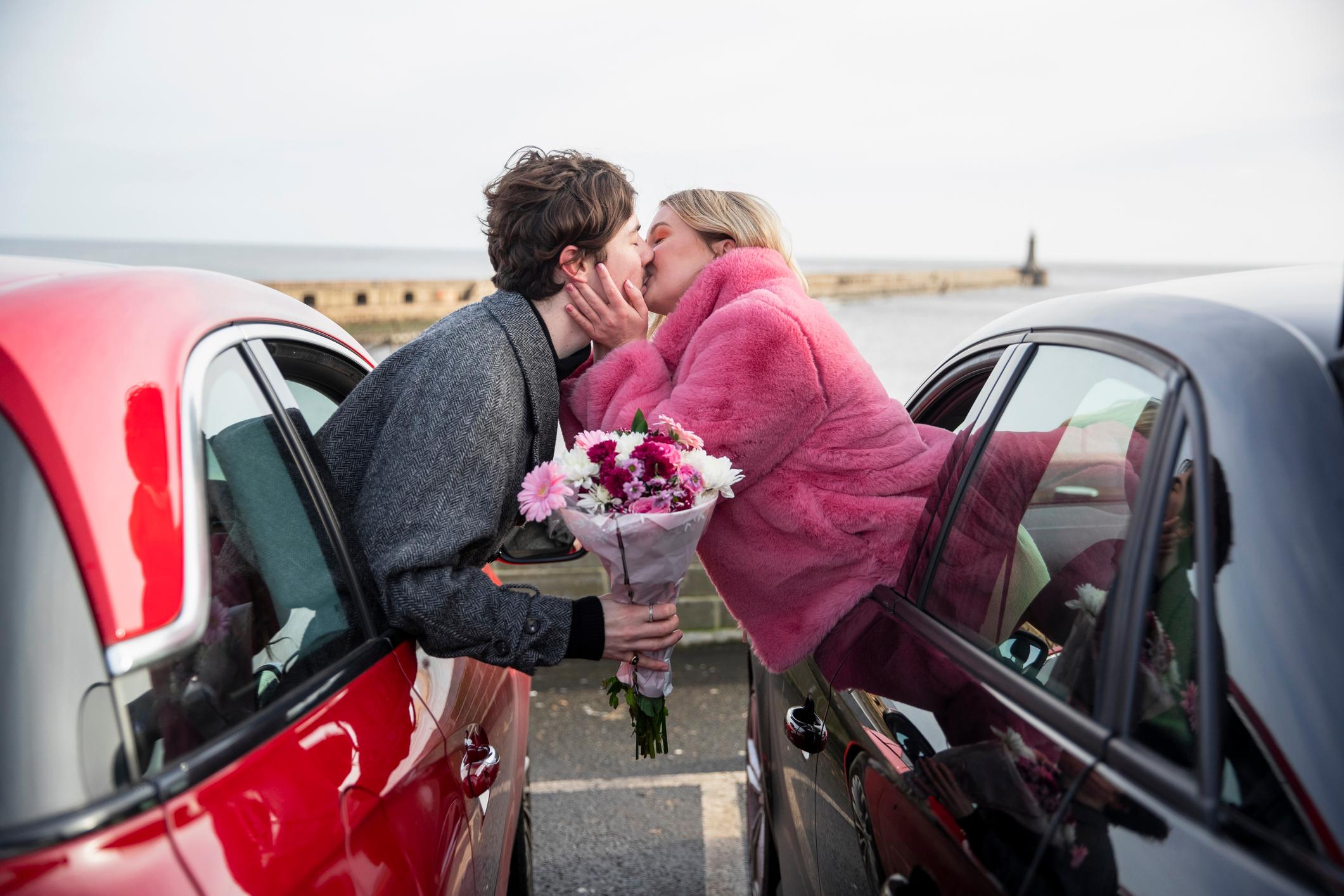 A man and a woman leaning out of a car window to kiss
