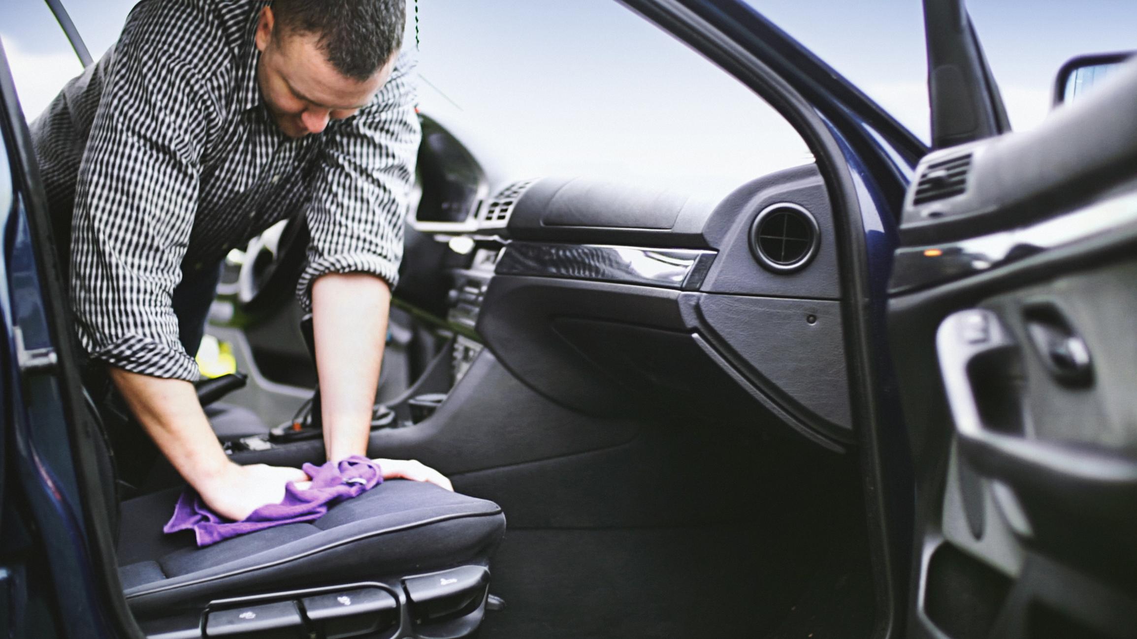 A man polishing the seats of a car with a purple cloth