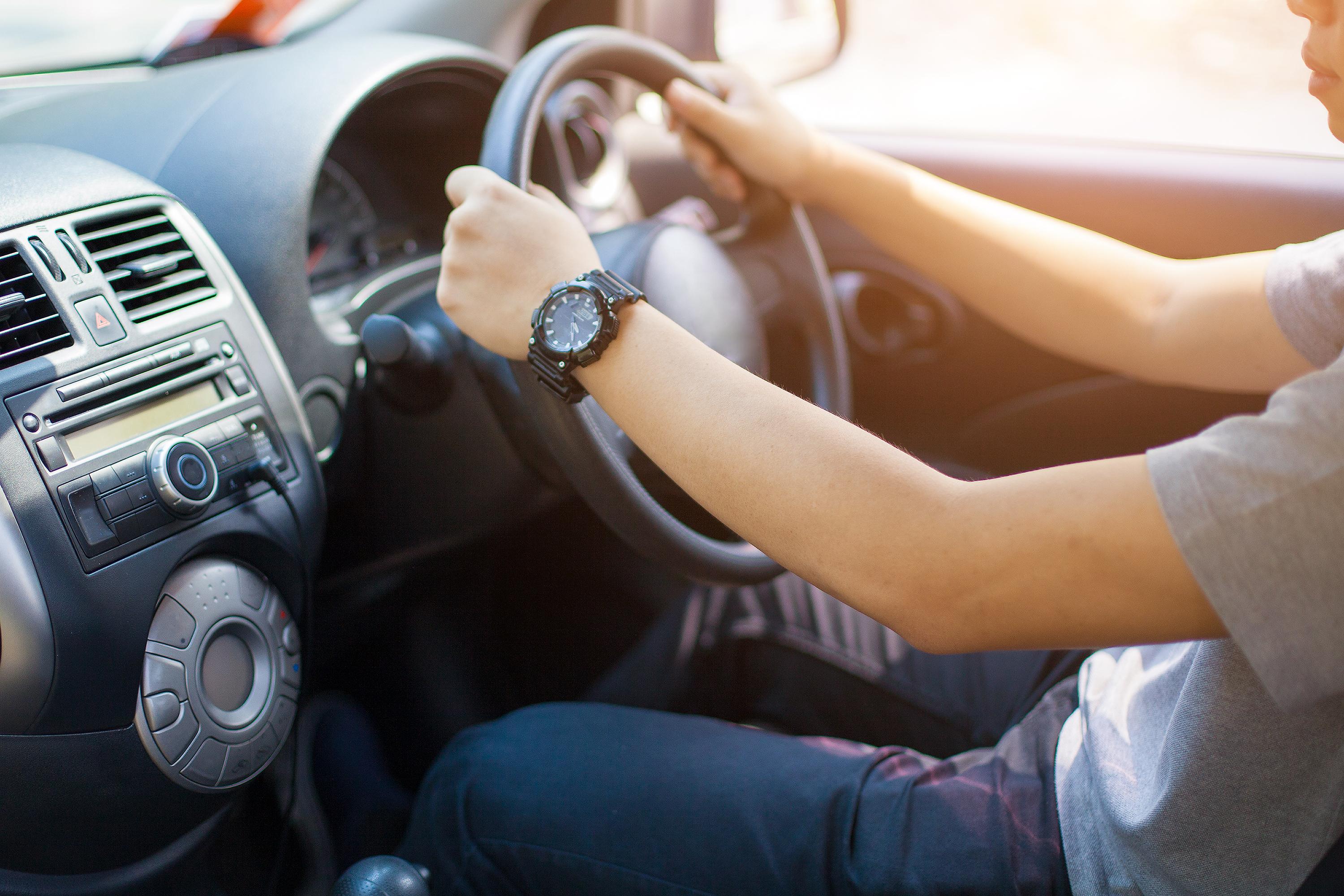 A close up shot of hands holding a steering wheel in the front of a car