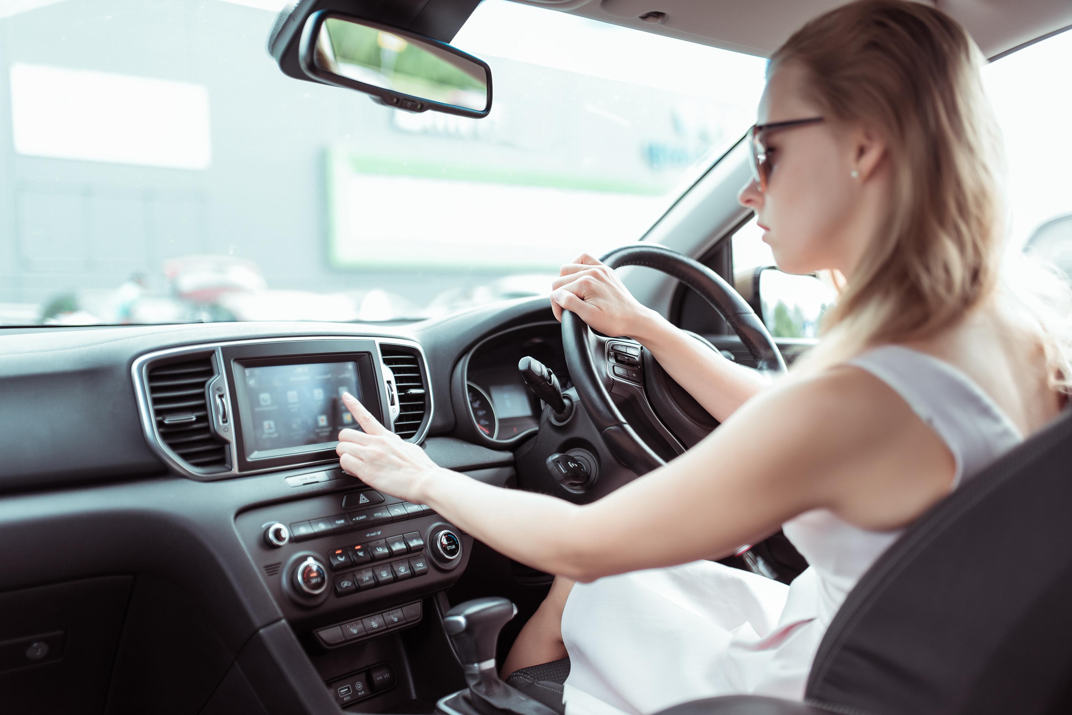 A woman in a white dress touching a car infotainment screen