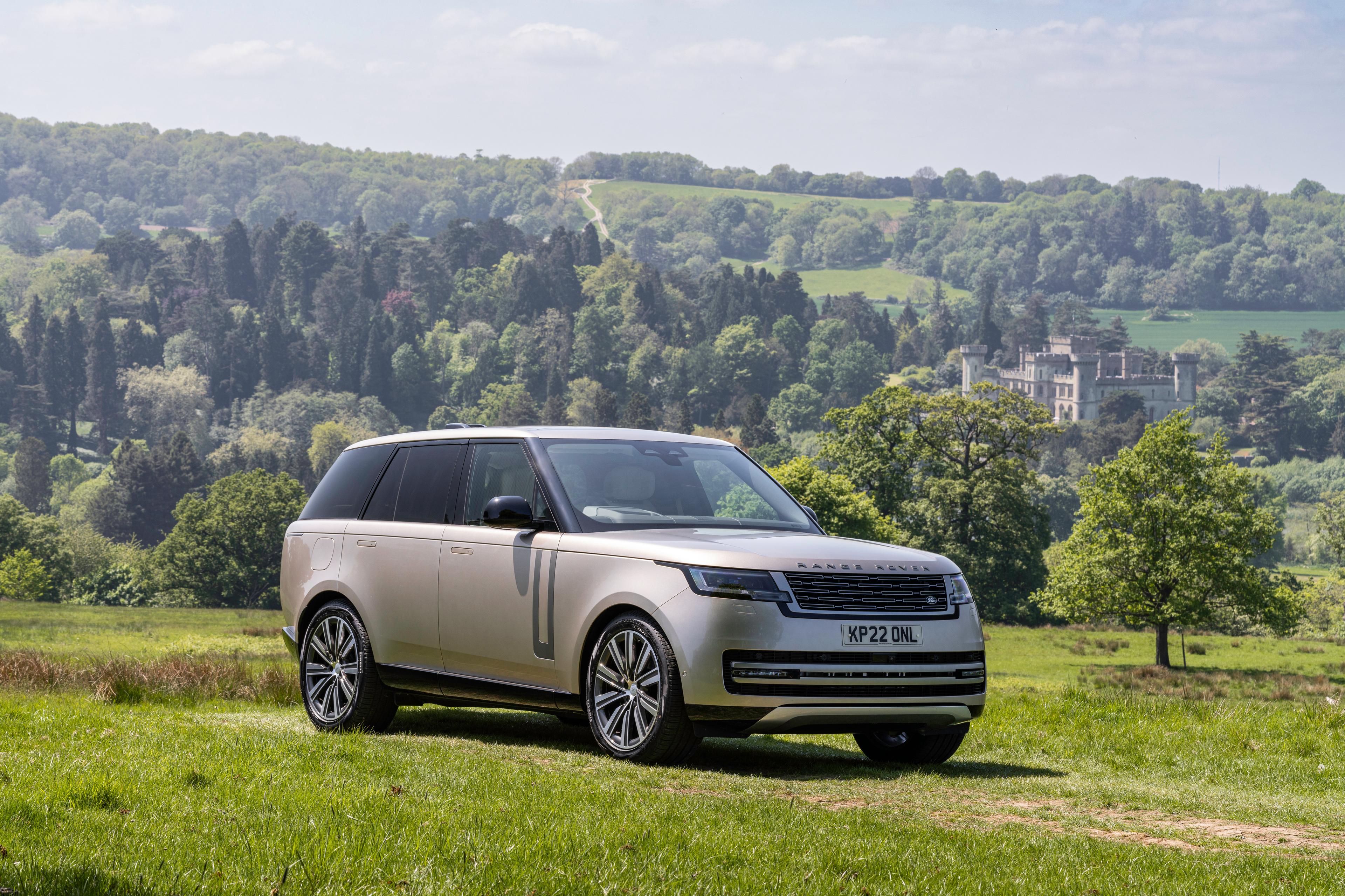 a gold range rover parked on grass in front of a hill