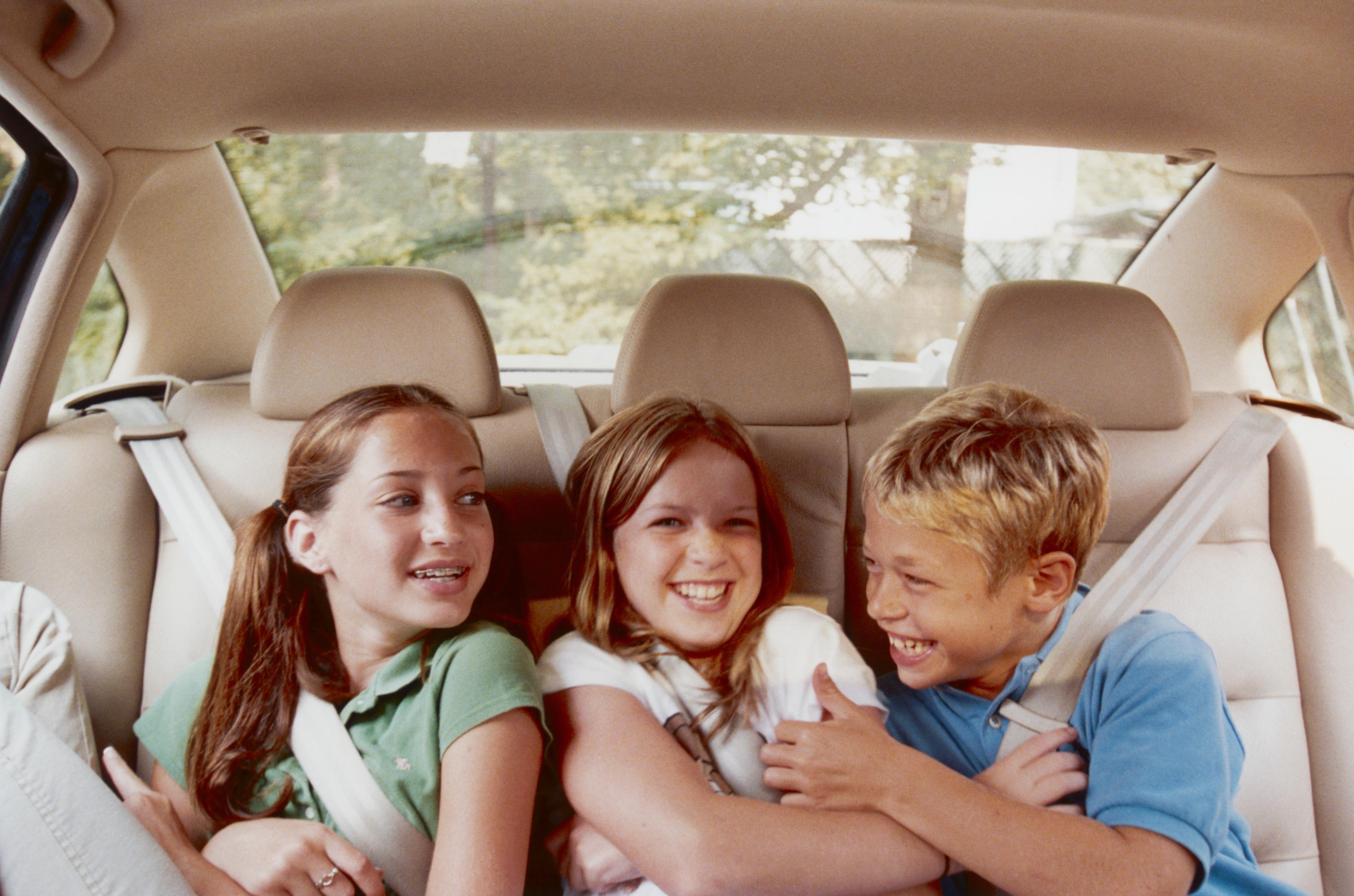 Three kids sat in the back of a car having a good time, sat on cream leather seats