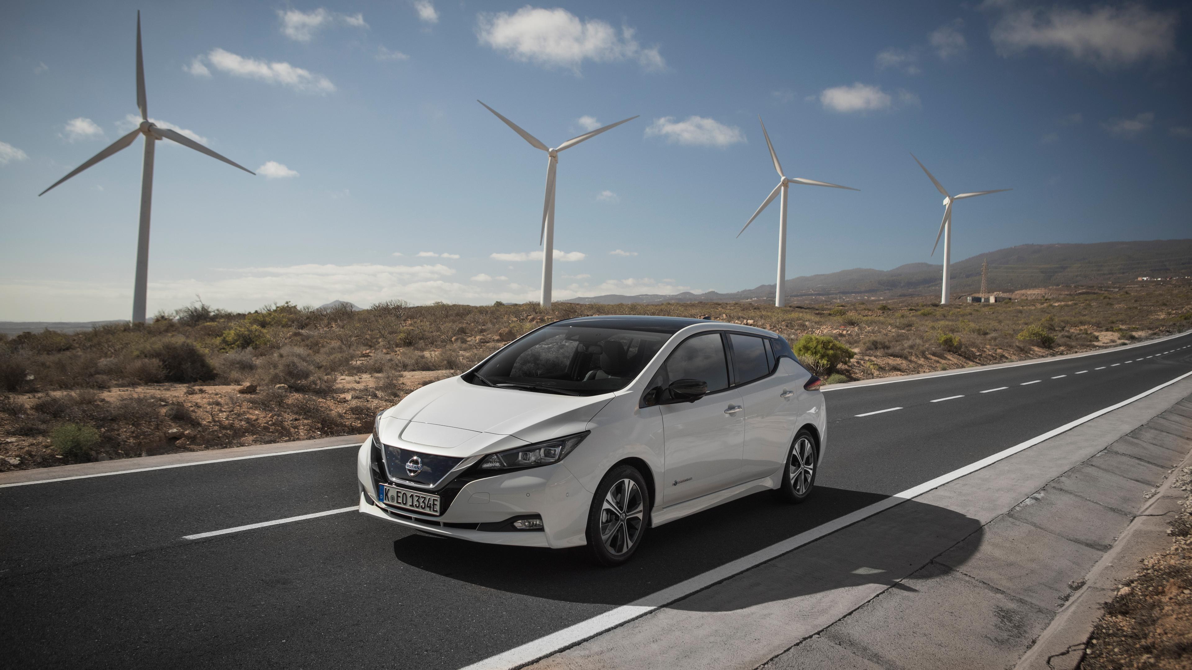 A Nissan Leaf electric car driving along a road lined with wind turbines