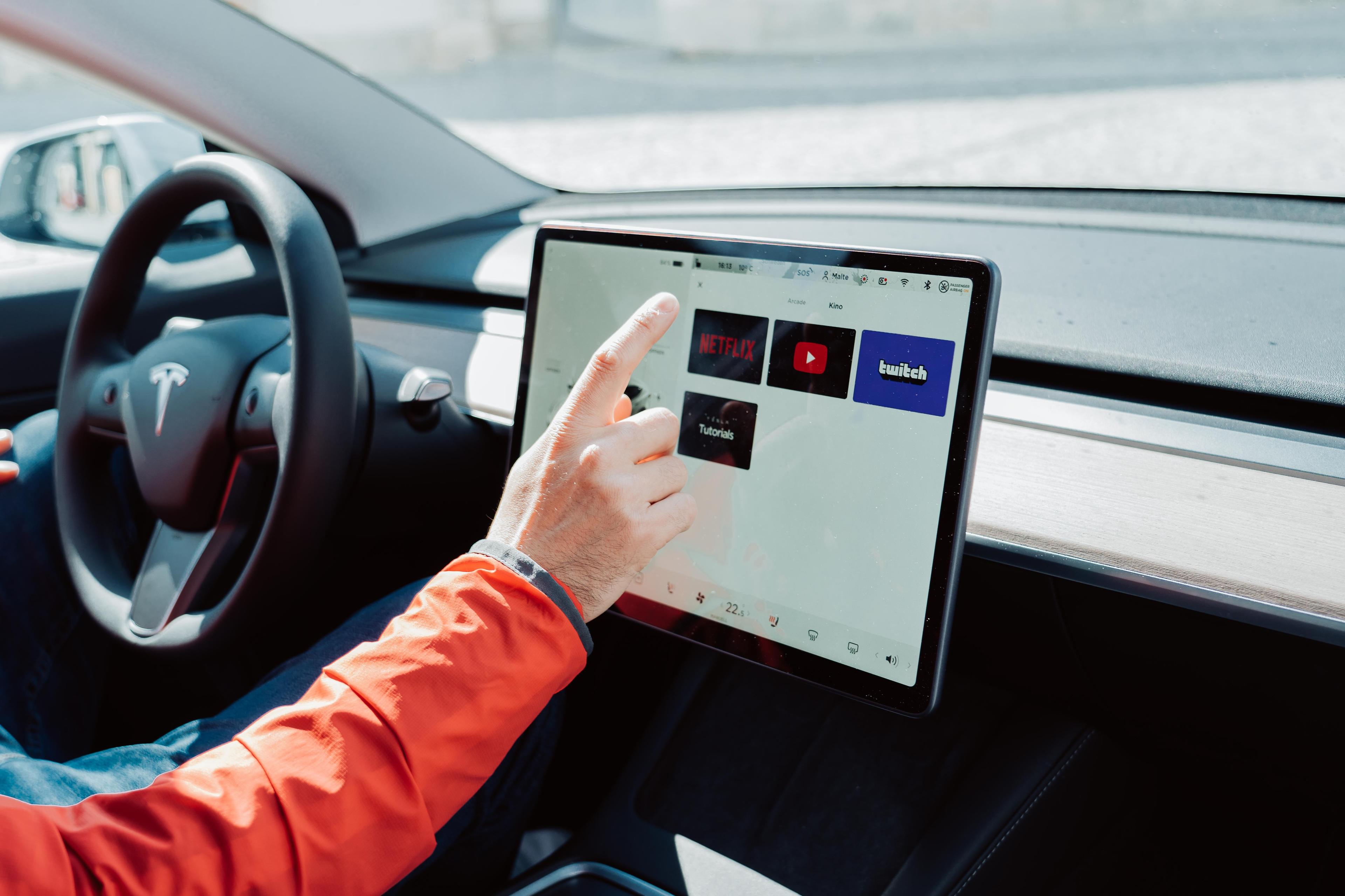 a man with an orange coat using the large touchscreen inside a Tesla Model 3