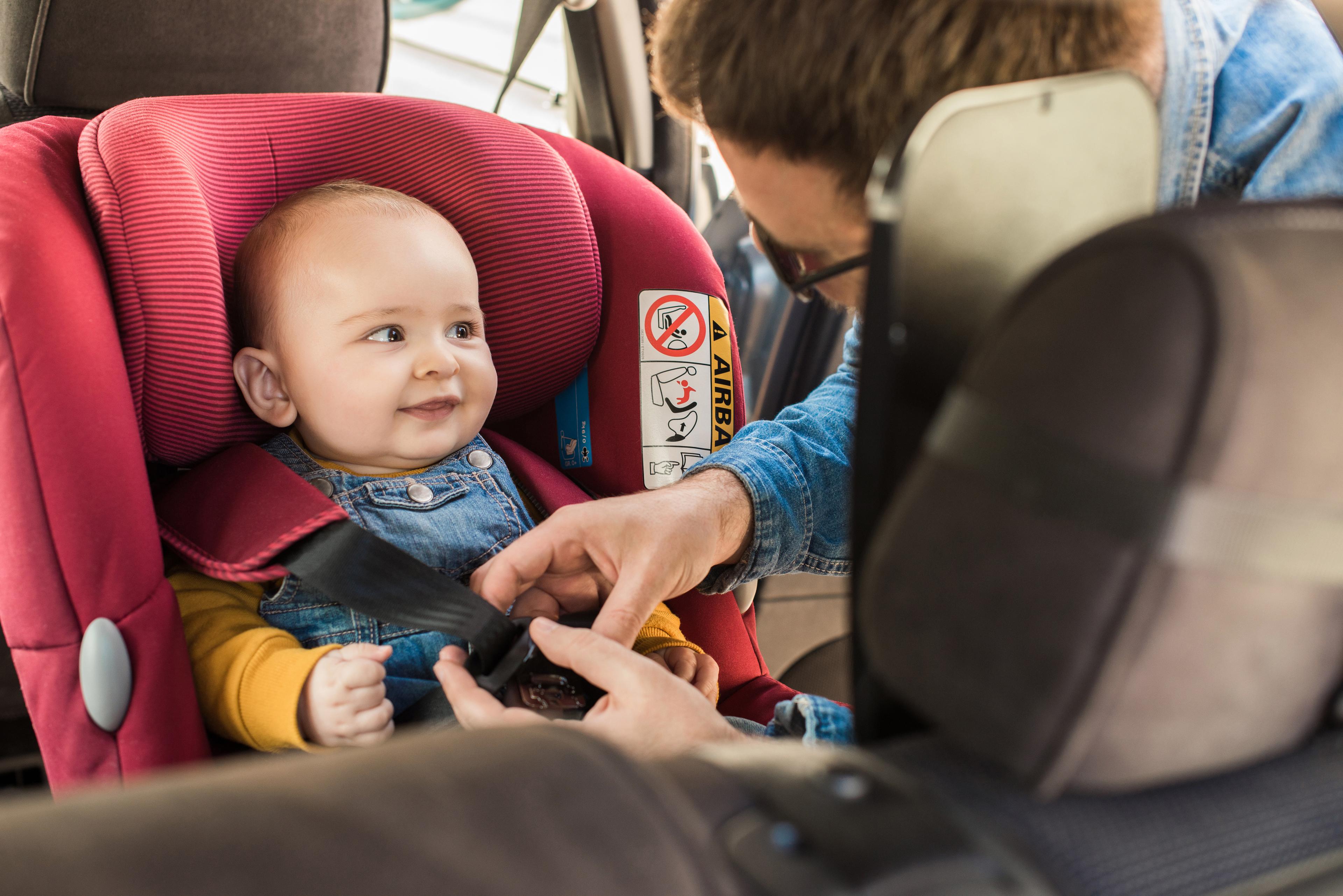 A smiling baby being strapped into an ISOFIX carseat