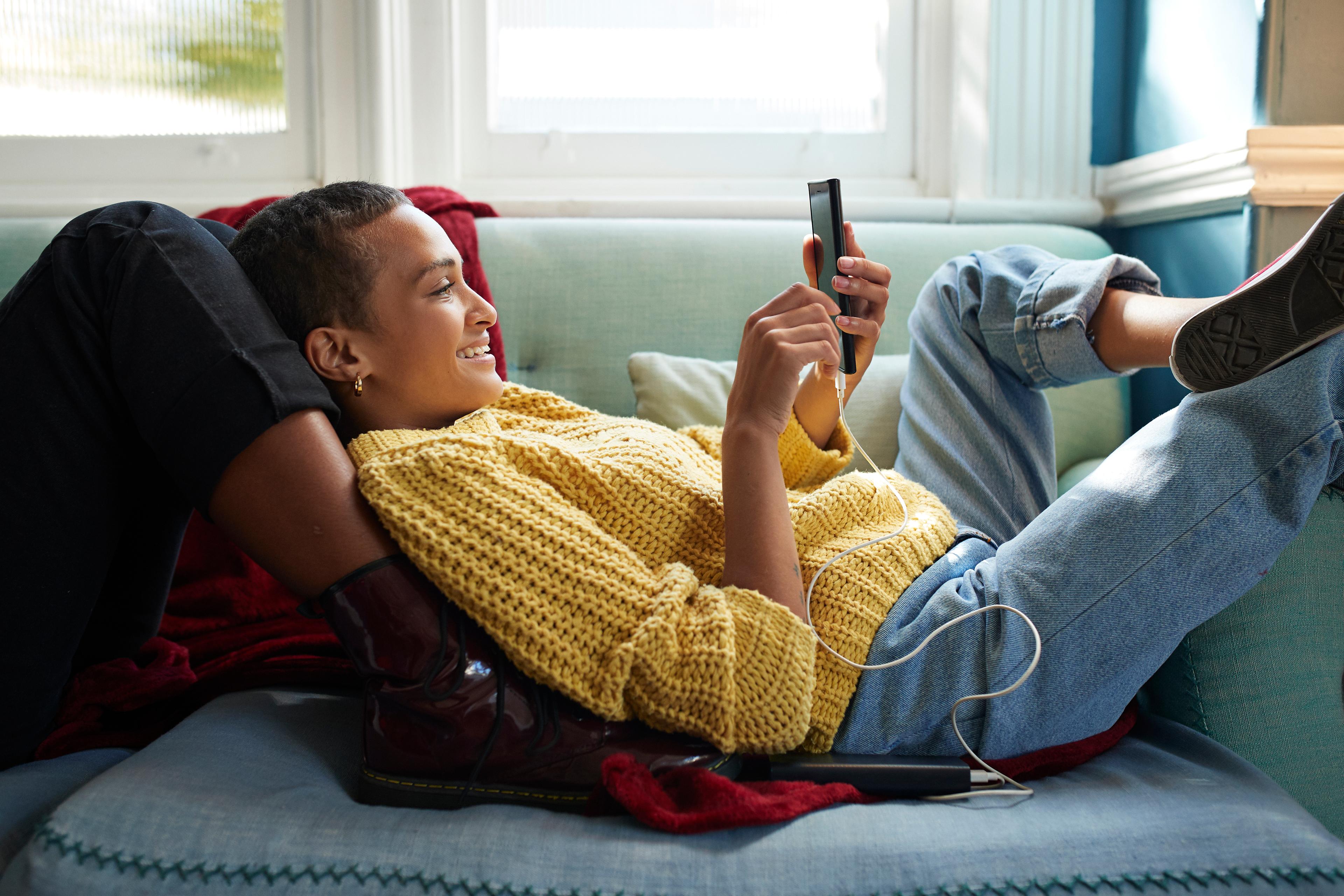 a woman lying on a duck egg coloured sofa wearing a knitted yellow jumper and looking at her phone