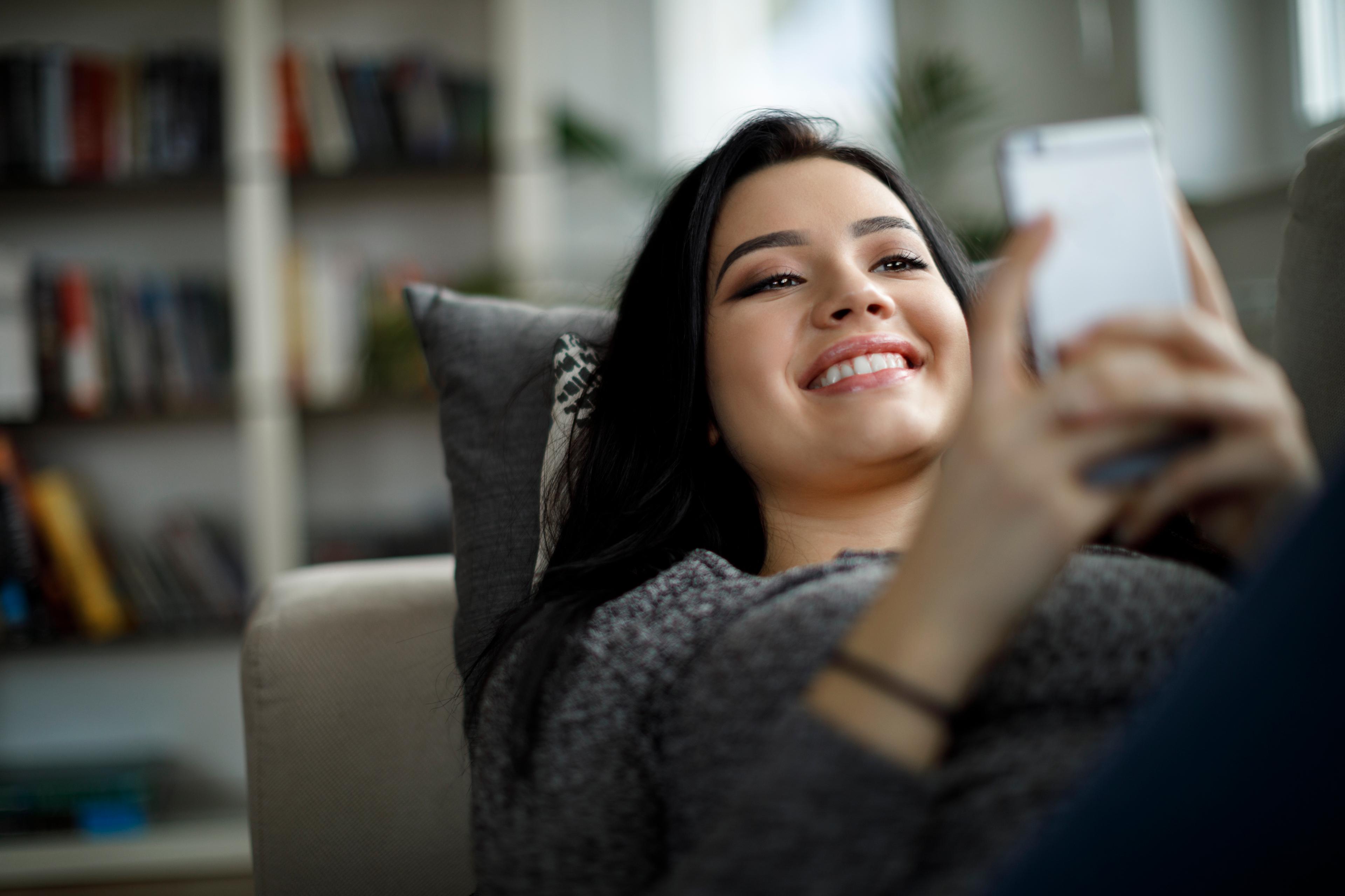 a woman lying down on a sofa smiling while on her phone